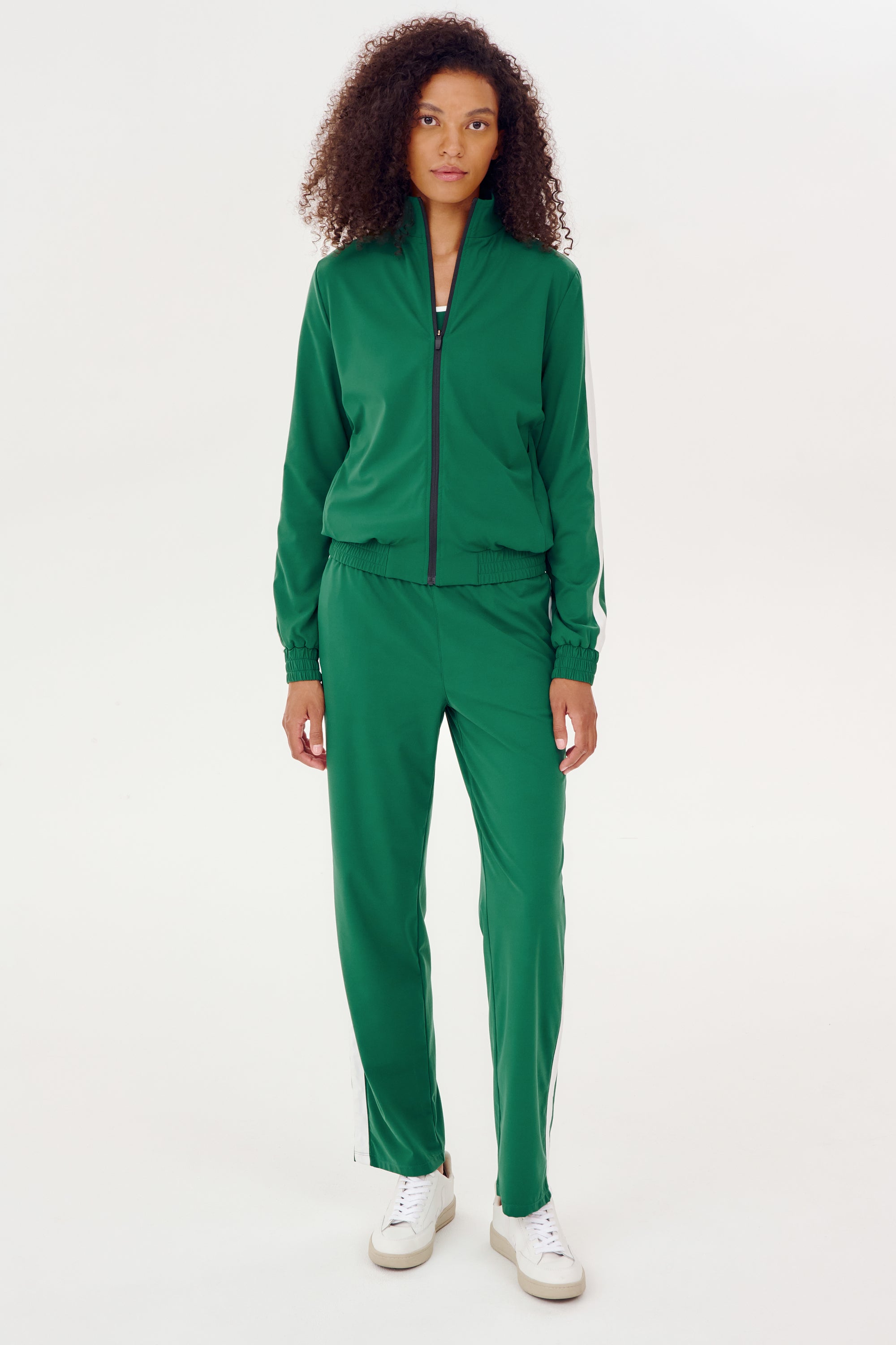 A woman warming up in a SPLITS59 Max Rigor Track Jacket in Arugula/White and white sneakers.