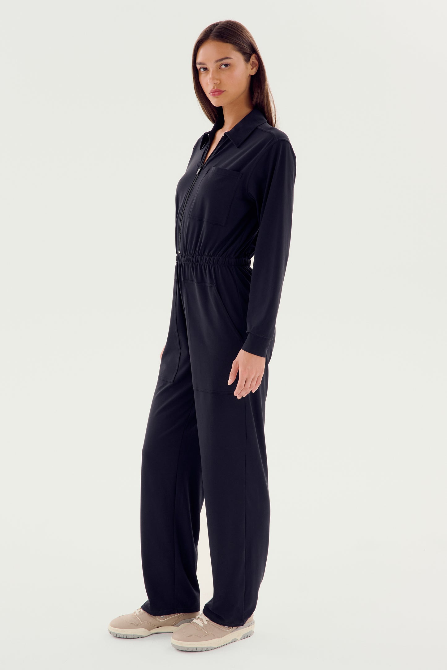 Wearing the Ollie Airweight Boiler Suit in black by SPLITS59, a person pairs it seamlessly with beige shoes against a plain light background.